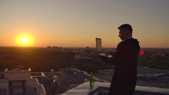 Hipster Man with a Laptop on the Edge of the Roof. Freelancer at Work. Wireless Mobile Internet. He alt