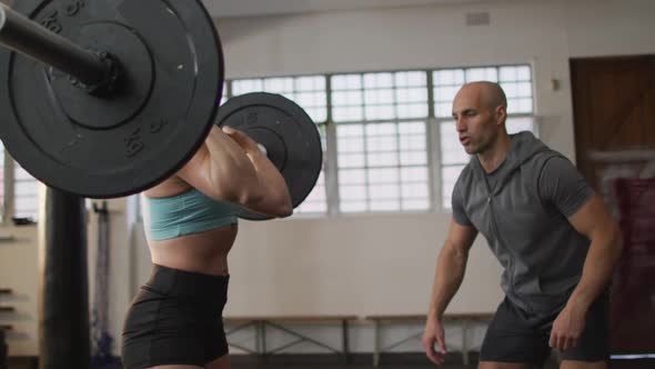 Fit caucasian woman working out with barbell with male trainer at the gym alt