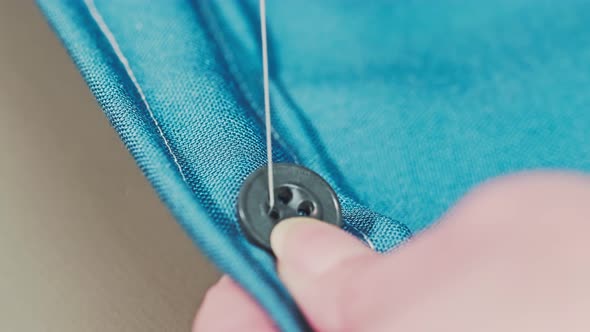 housewife's hands are sewing on a button. Repair of clothes at home.