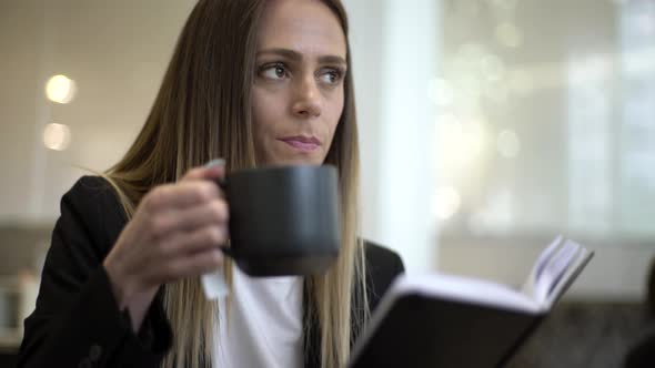 Businesswoman drinking coffee and reading diary alt
