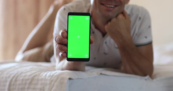 Man Lies on the Bed Holds a Phone in His Hand with a Green Screen