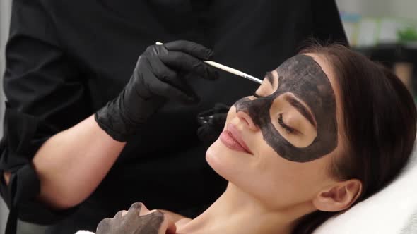 Cosmetologist Applying Black Mask on Woman Face with Brush alt
