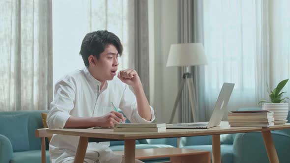 Asian Man Student Being Sleepy While Using Computer To Study Online At Home alt