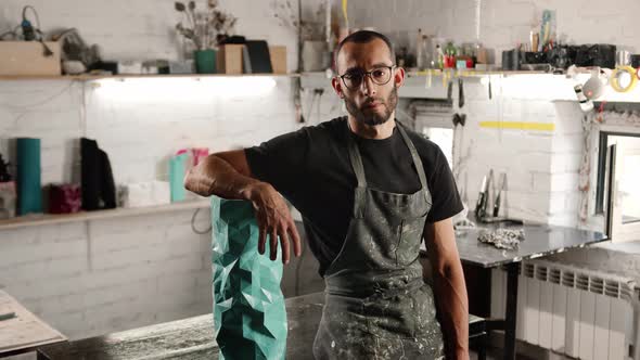 Portrait of a man: a male artisan sculptor looks at the camera against the backdrop of a workshop alt