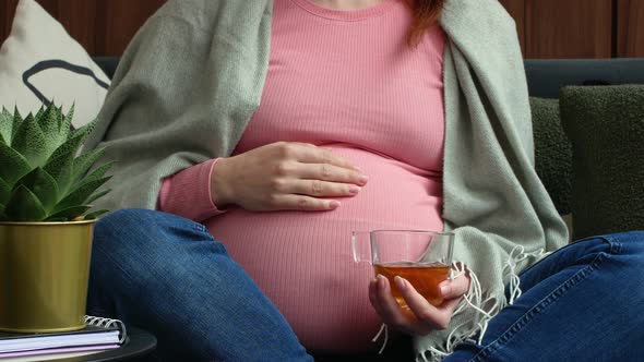 Pregnant woman drinking a healthy herbal tea, wrapped in a warm plaid.