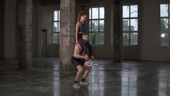 Athletic Shirtless Man Crouches with a Girl on His Shoulders in Empty Loft Studio alt