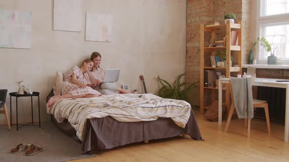 Twin Sisters Using Laptop on Bed alt