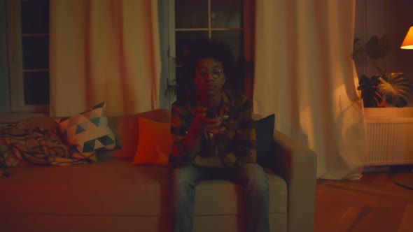 African Man Switching Tv Channels with Remote Control Sitting on Sofa at Home alt