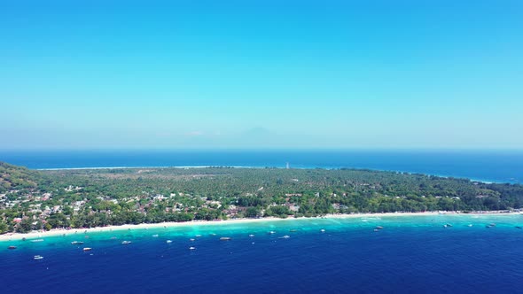 Blue Calm Sea With Green Trees and Clear Blue Sky In the Background - Aerial Shot alt