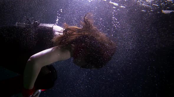 A Beautiful Woman Is Deep Under the Water on a Dark Background Floating Creating a Lot of Bubbles alt