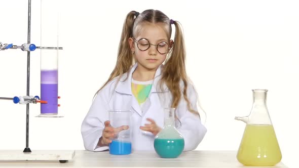 Cute Girl with Ponytails in Uniform and Round Glasses Evaluates, Mixing, Standing By the Table alt