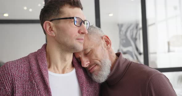 Gay LGBT Man Puts Head on Shoulder of Partner Hugging at Home
