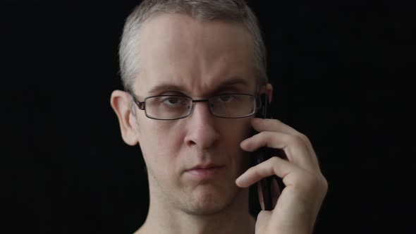 a Man with Glasses Talking on the Phone and Cursing on a Black Background