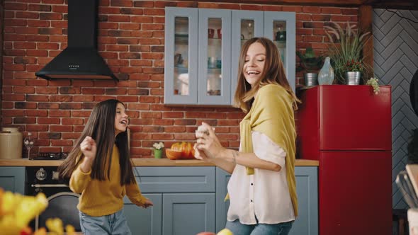 Young Overjoyed Mum and Little Daughter are Laughing and Dancing While Cooking in Modern Kitchen at alt