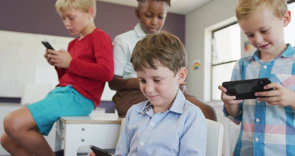 Video of diverse boys sitting at school desks and playing games on smartphones alt
