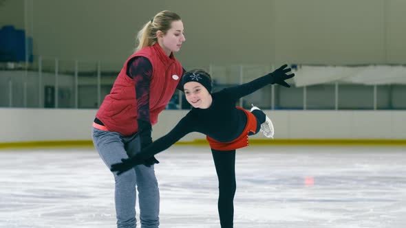 Professional trainer helping figure skating girl to do arabesque