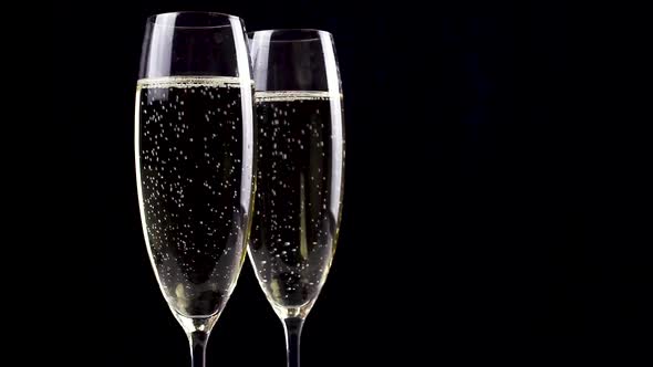 Two glasses of champagne with bubbles on black background.