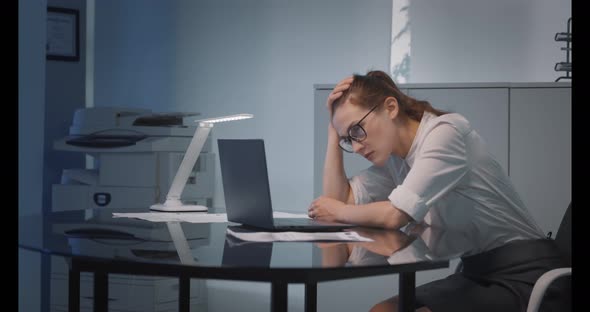 Young Tired Businesswoman Looking Unhappily at Laptop Display Analyzing Financial Data in Office alt