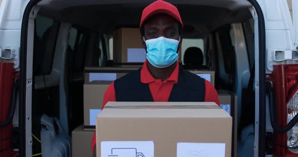 African man courier delivering packages with truck while wearing safety face mask alt