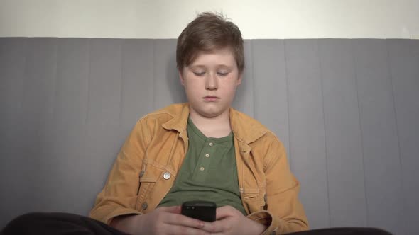 Boy using smartphone at home and looking at camera