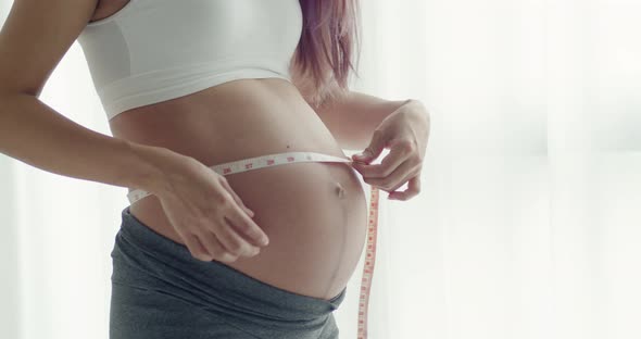 Young Asian Pregnant woman measuring her belly with a tape.