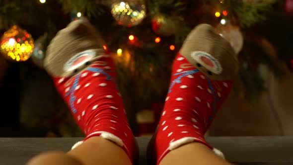 Woman legs in cozy Christmas socks with a deer on the background of a decorated Christmas tree