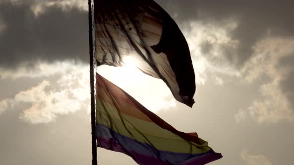 Rainbow LGBT gay pride flag waving in the wind 4 and the American flag waving with sun backlit under alt