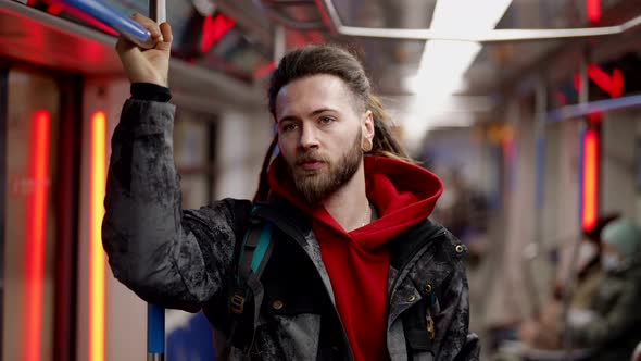 A Handsome Bearded Man with Dreadlocks Standing in Public Transport Holding on to the Handrail with alt
