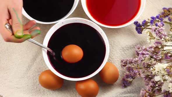 Caucasian Child Paints an Easter Egg with a Metal Spoon and Dips It Into a White Bowl with Red Dye alt