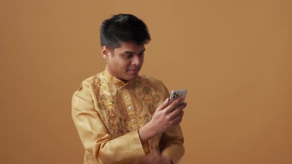 Cheerful Indian man in national cloth looking at phone alt