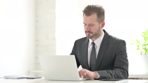 Young Businessman Pointing at Camera While Using Laptop in Office alt