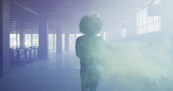 Mixed race woman holding green flare walking through empty building alt