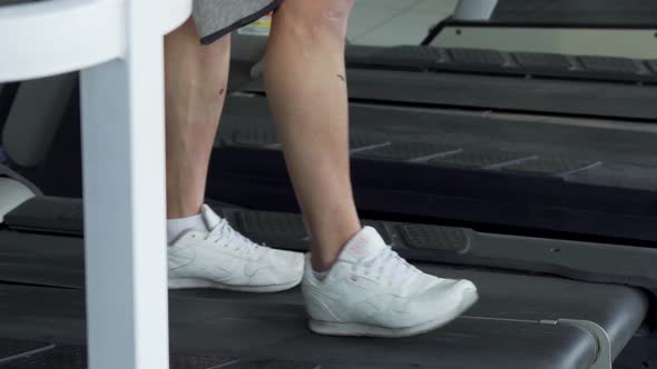 Unrecognizable Man Using Smart Phone While Walking on a Treadmill at the Gym alt