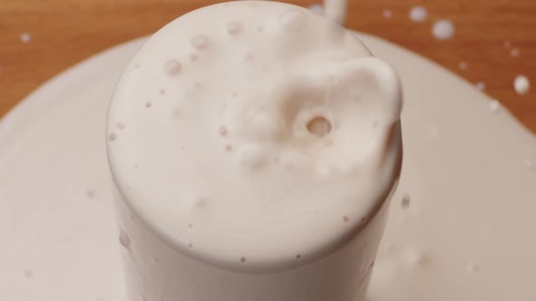 Yoghurt Pouring Into a Glass and Brim Over the Edgeon Table Close Up