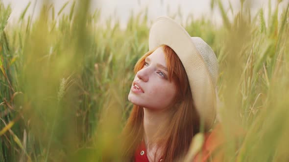 Close Up Slow Motion of Romantic Redhead Girl in Straw Hat and Red Dress Standing in Wheat Field and