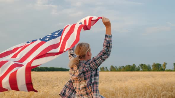 Back View of Woman with USA Flag Runs in the Sun on a Wheat Field alt