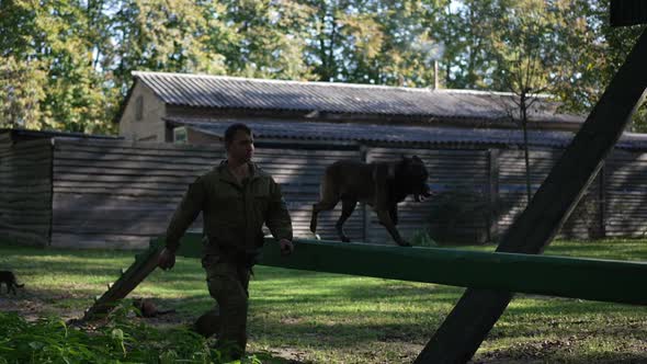 Tracking Shot Dog and Caucasian Man Running Outdoors on Lawn with Barriers in Slow Motion alt