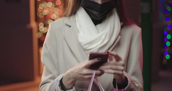 Woman typing on a smartphone wearing a surgical mask.