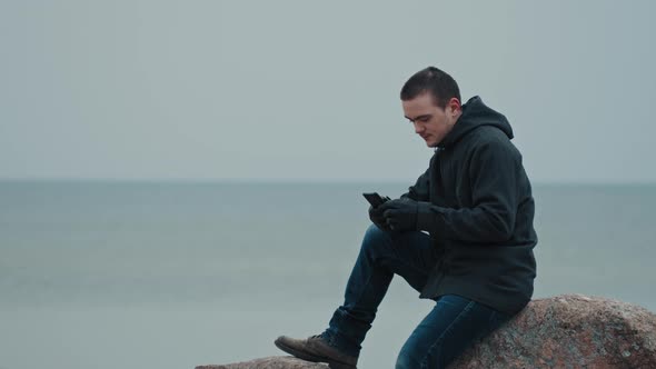 A young guy is sitting on a stone against the background of the blue sea