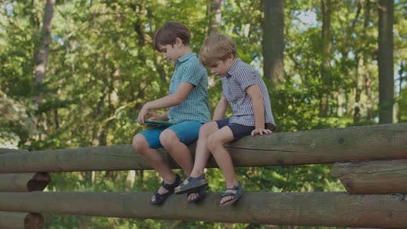 Two Kids with One Gadget Outside. Older Brother Using Tablet Computer, Younger Brother Is Offended.