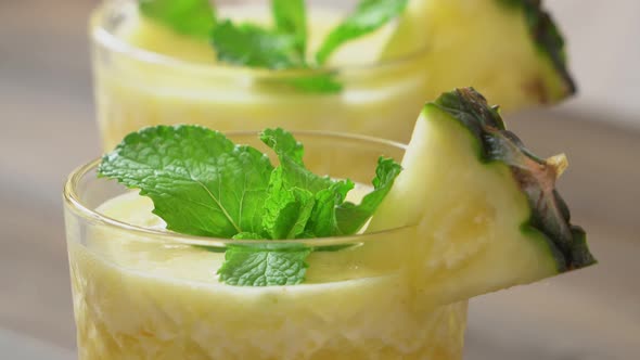 Healthy homemade pineapple fruit smoothies in the glasses being garnished with peppermint leaves