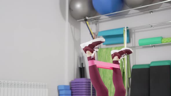 a Woman Does Exercises for the Legs with Gymnastic Elastic Bands on a Mat alt