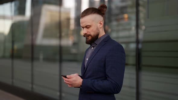 a Mustachioed and Bearded Businessman in a Plaid Jacket is Standing with a Phone in Hands and Typing alt