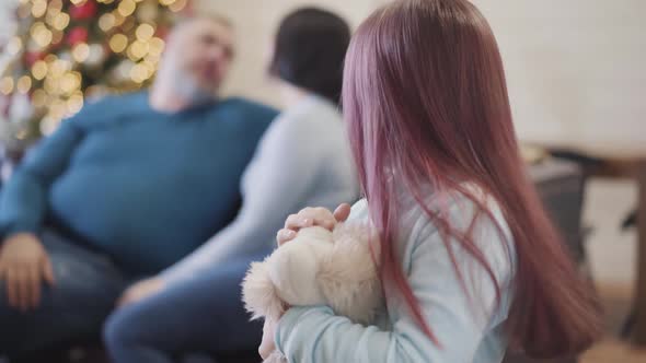 Beautiful Little Girl Looking Back at Blurred Parents Sitting at the Background and Turning To alt
