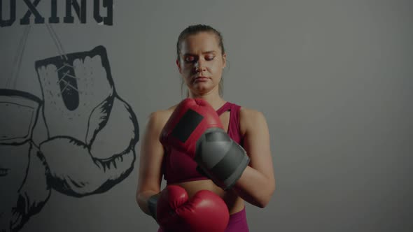 A sporty woman puts boxing gloves on her hands before training in the gym alt