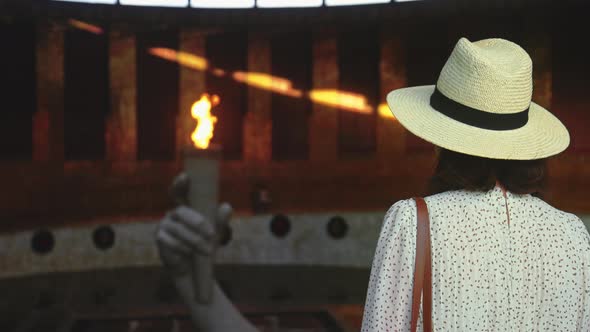 A young girl in a hat looking at the eternal flame in the pantheon alt