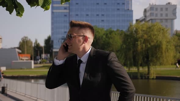 A Successful Businessman Rides a Gyro Scooter in a Park and Talks on the Phone alt