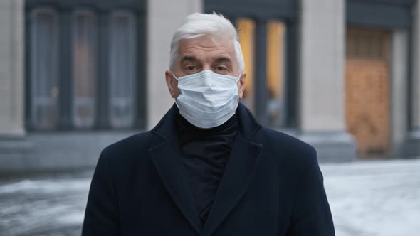 Old Graying Man in Coat and Covid 19 Face Mask Walks on Epidemic European Street