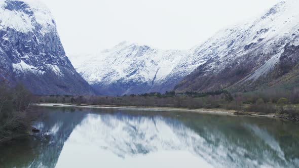 Picturesque Snow Capped Mountains of Trollveggen Reflected In Clear Lake In Norway - aerial shot alt