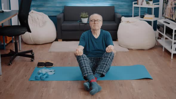 Old Person Sitting in Lotus Position with Closed Eyes on Mat alt
